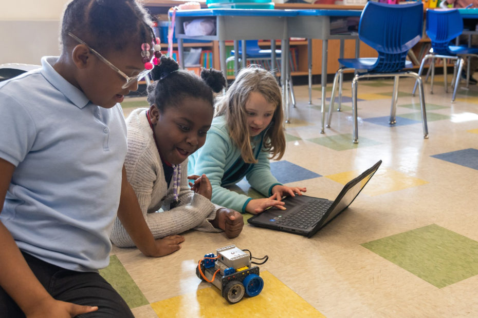 3 students interacting with a VEX GO Robot and using a laptop.