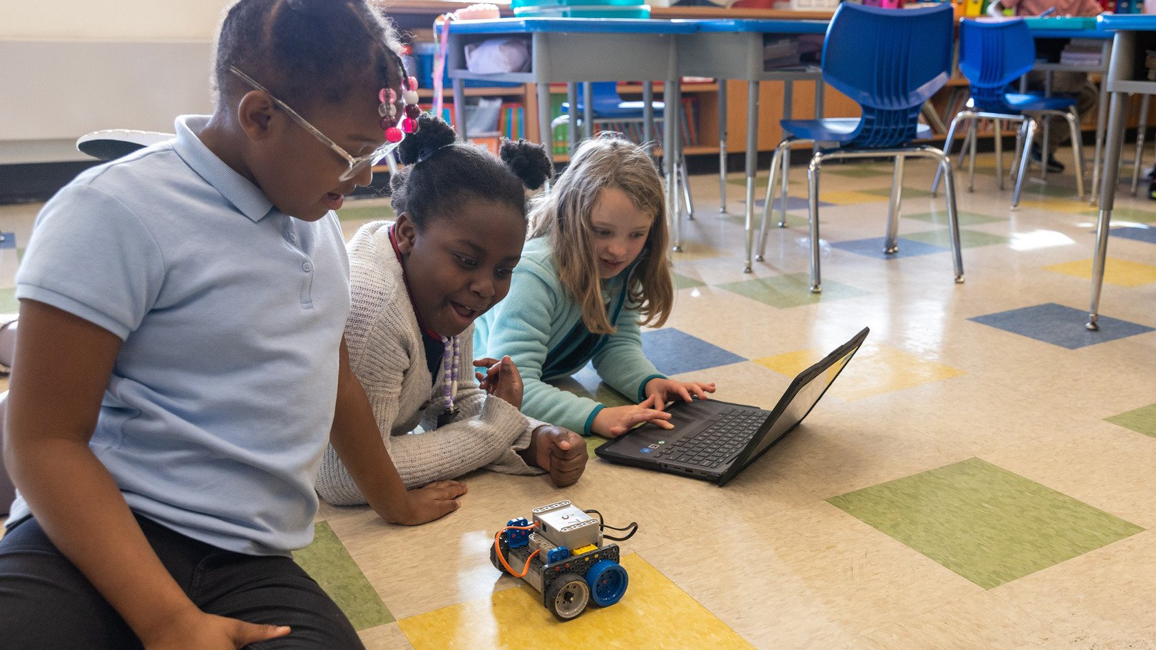 3 students interacting with a VEX GO Robot and using a laptop.