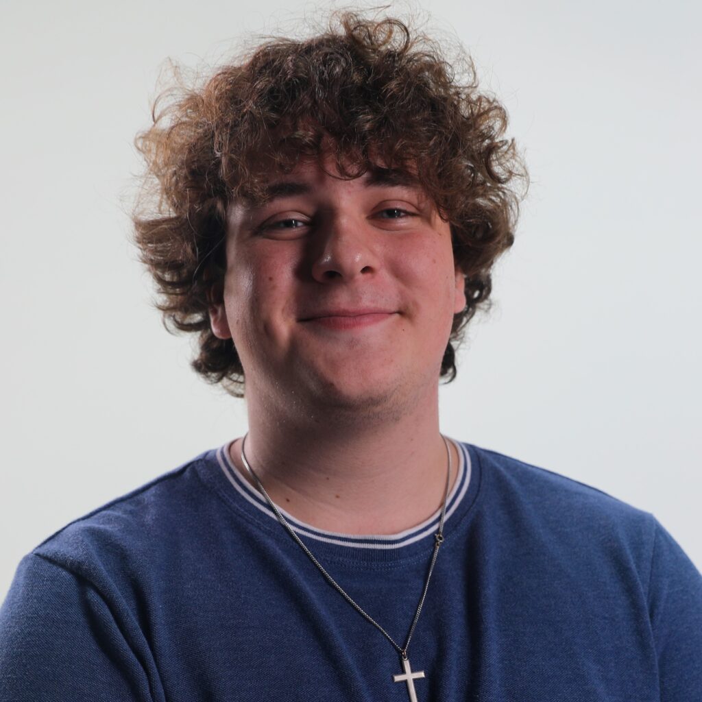 An intern, Aidan, smiling. He has brown curly hair and a blue shirt.