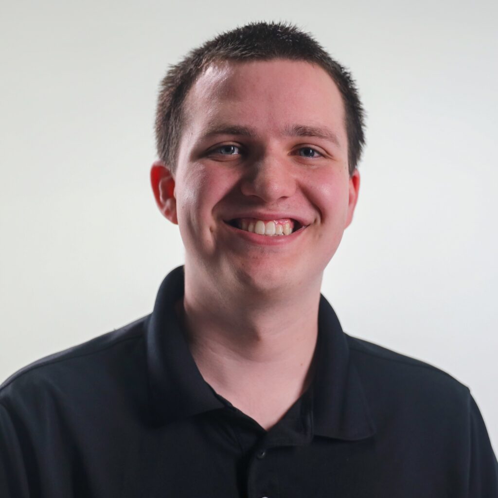 An intern, Brandon, smiling. He has close cropped black hair and a black polo shirt.