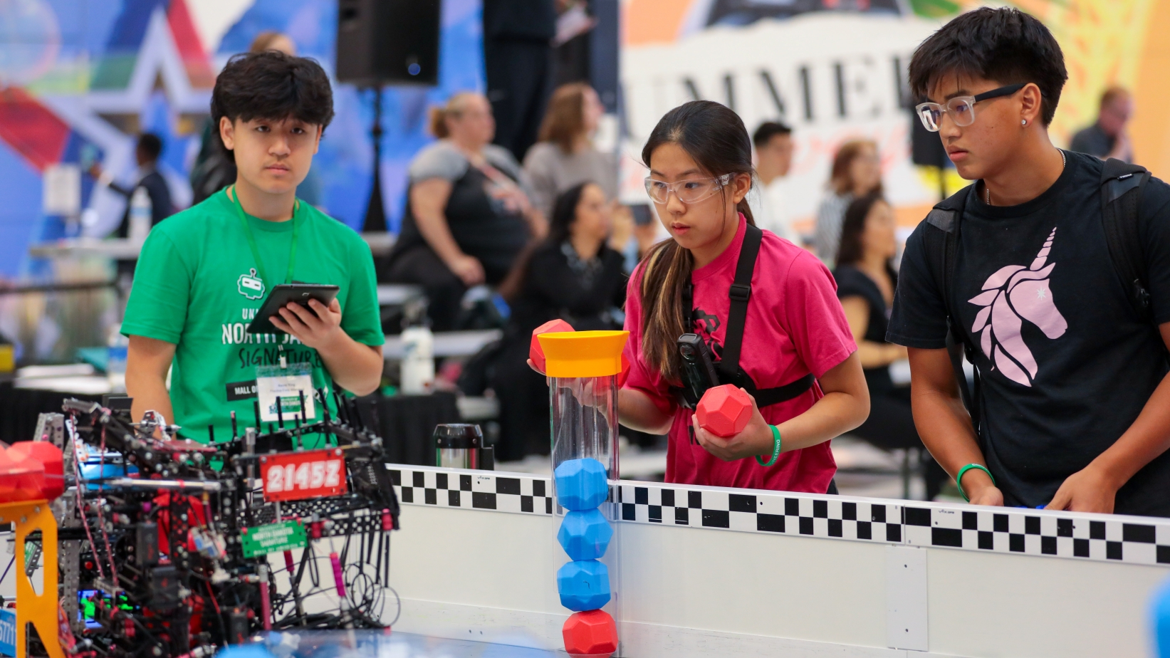A student in a pink shirt prepares to load during a Push Back match at the 2025 UND Signature Event at the Mall of America. A team mate stands to her left and a volunteer to her right.