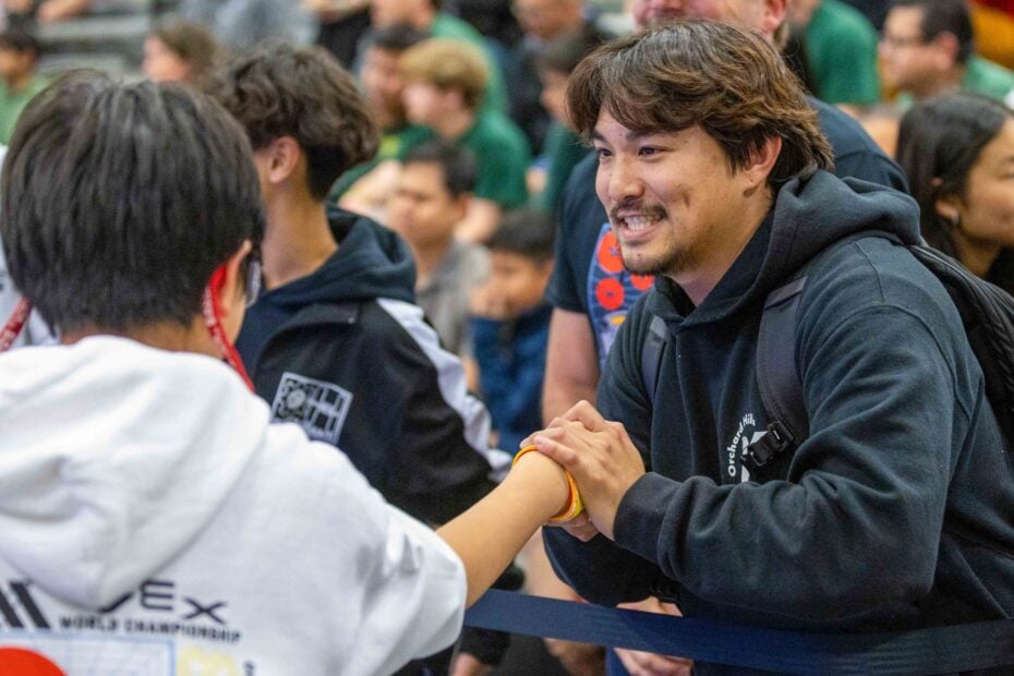A coach in a black hoodie proudly shakes the hand of a student in a white hoodie.