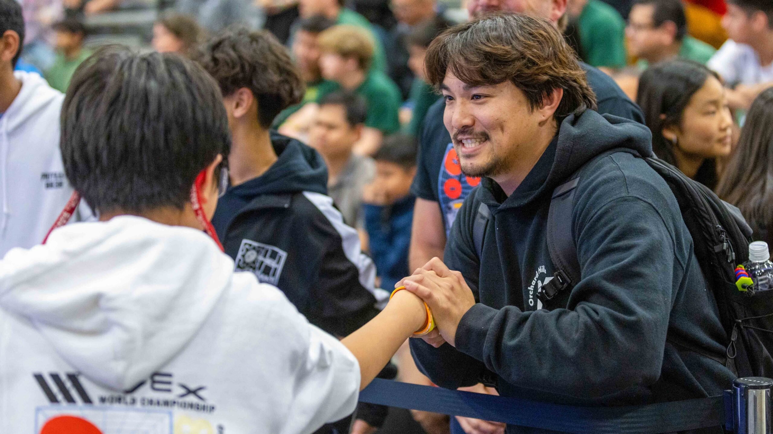 A coach in a black hoodie proudly shakes the hand of a student in a white hoodie.