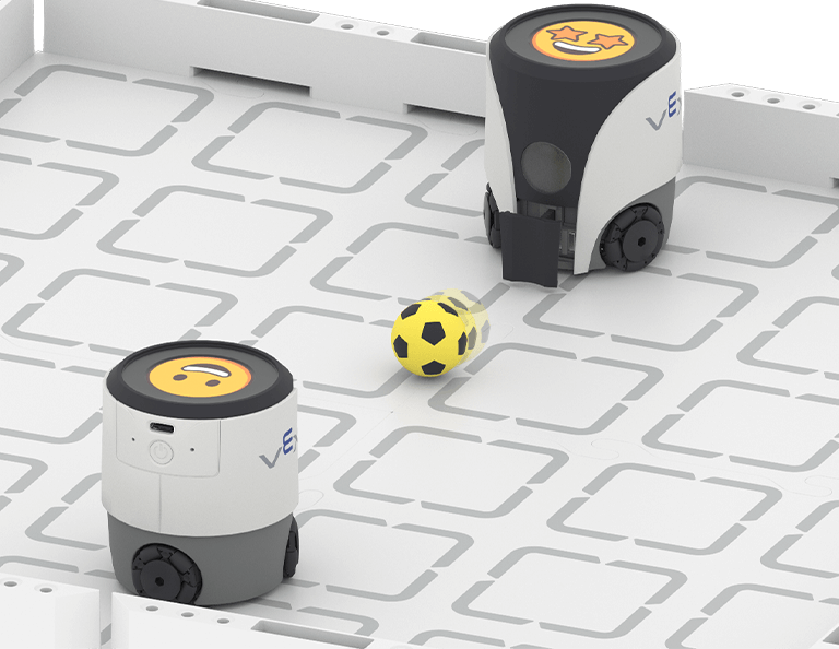 Two VEX AIM robots displaying happy emojis are on a white and grey field. The further away one shoots a soccer ball towards the other.