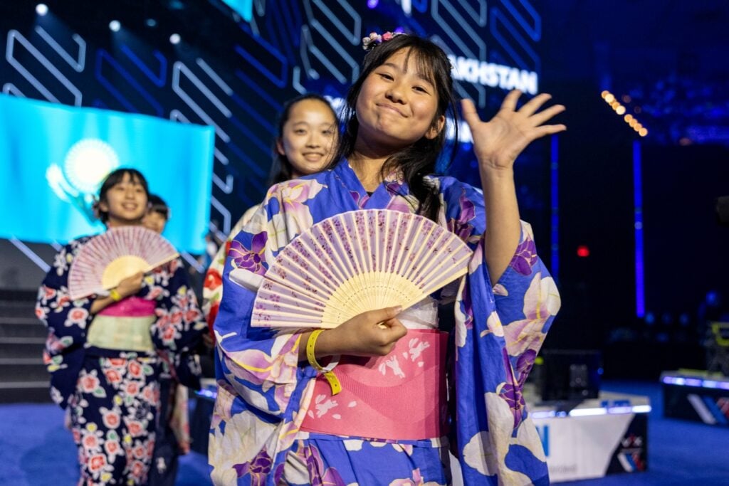 A member of Team DamBare smiles and waves at the camera while walking in the Parade of Nations at the 2025 VEX Robotics World Championship.