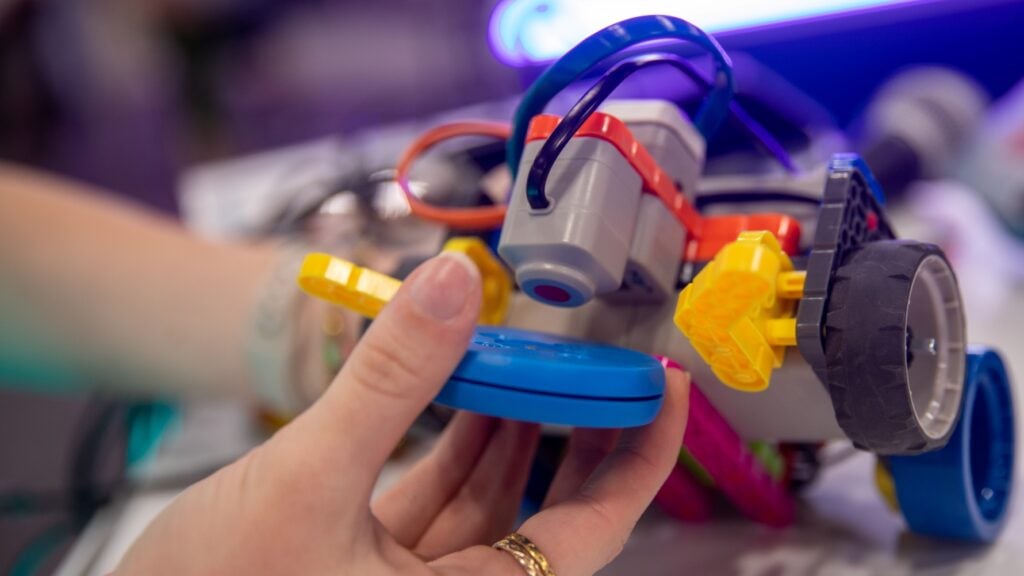 A hand holds a blue disk up to a VEX GO robot's magnet.