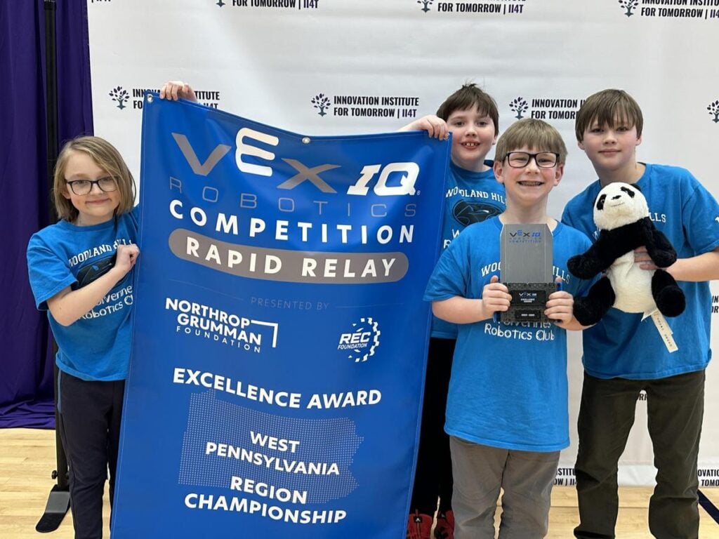 The 4 members of the IQ Pandas hold a banner they won for an Excellence Award at the 2025 West Pennsylvania Region Championship.