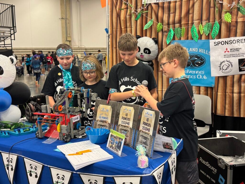 The 4 members of the IQ Pandas smile pass a microphone while being interviewed at the 2025 VEX Robotics World Championship.