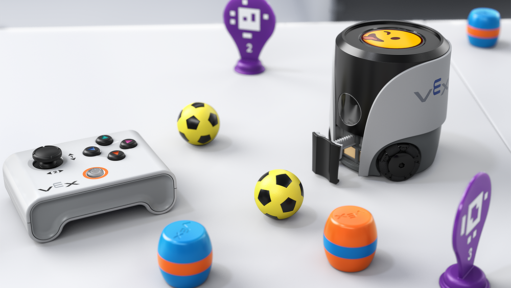 A VEX AIM robot appears on a white table with an emoji with its tongue out on its screen. Around it are AprilTag signs, soccer balls, barrels, and a controller.