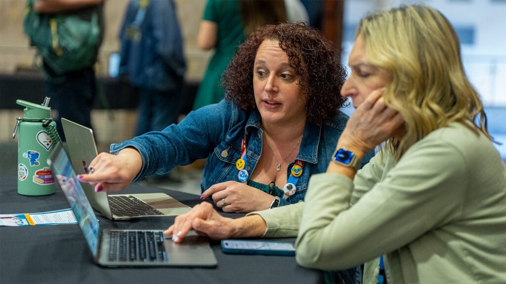 An attendee speaks with VEX Robotics Senior Education Developer Audra Selkowitz, who points at a laptop screen.