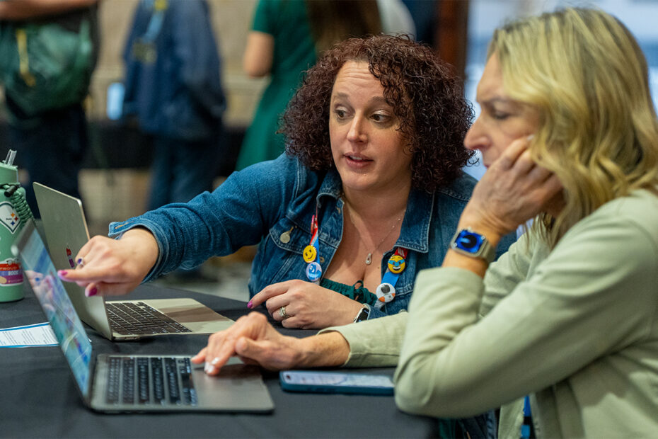 An attendee speaks with VEX Robotics Senior Education Developer Audra Selkowitz, who points at a laptop screen.