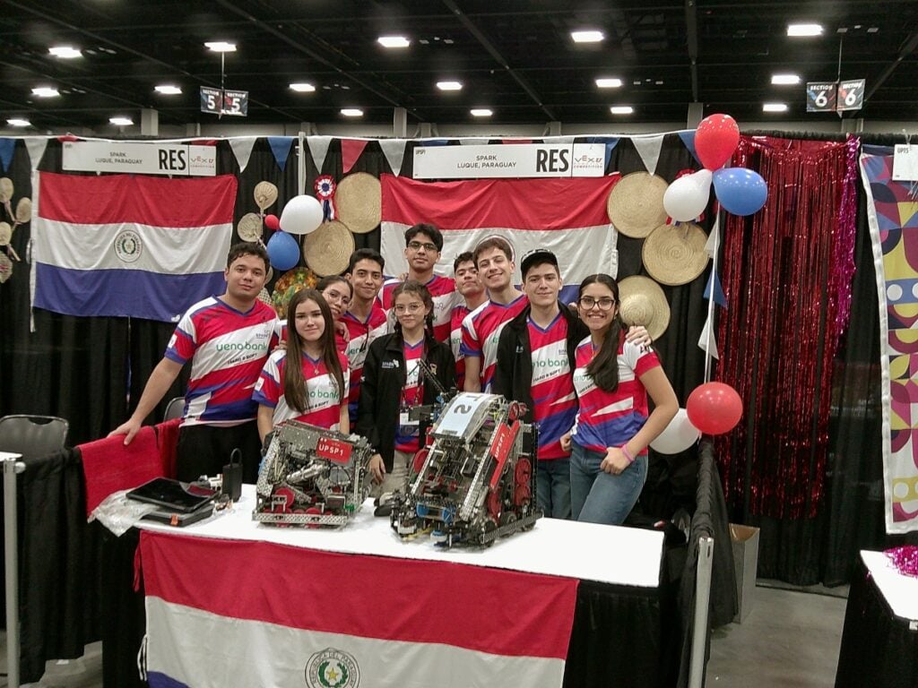An image by Team UPSP SPARK of the team standing in front of their pit area decorated with balloons and Paraguayan flags.
