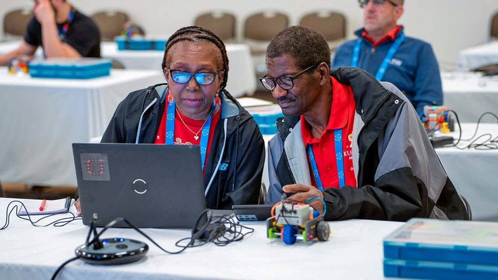 Two educators lean over a computer next to a VEX GO robot.
